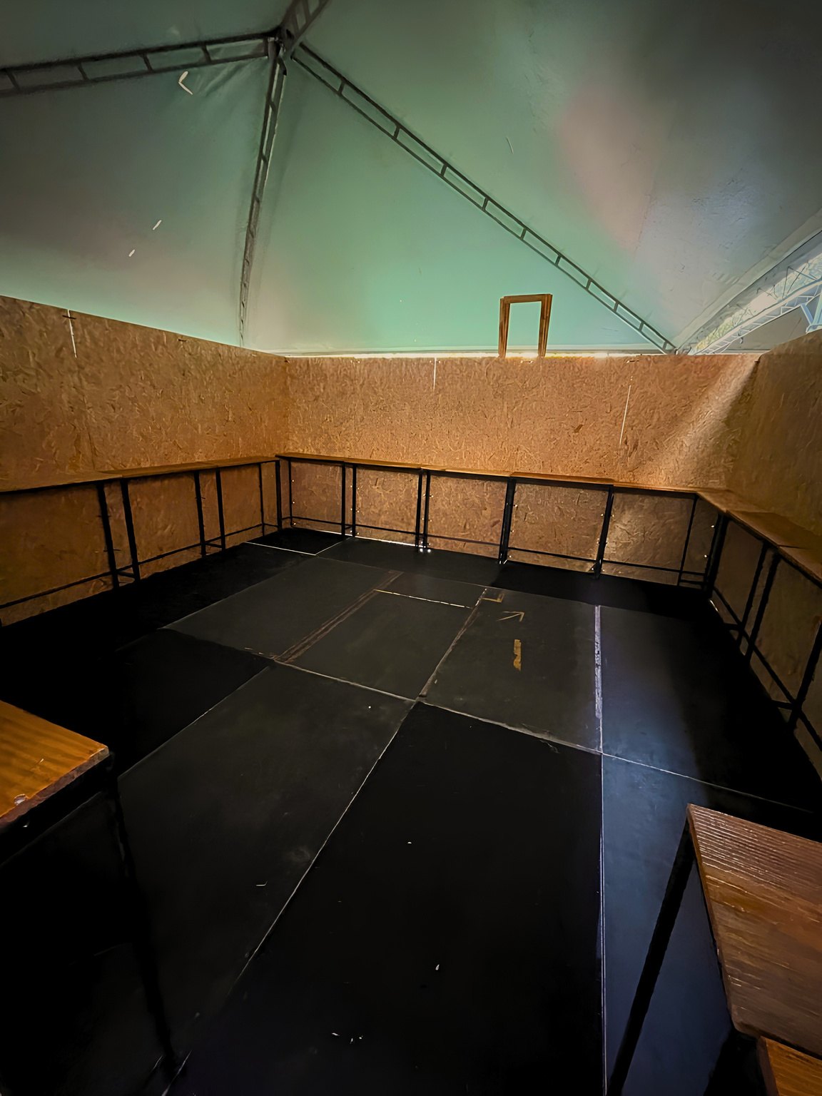 Espaço modular com paredes de madeira e piso preto montado sob tenda