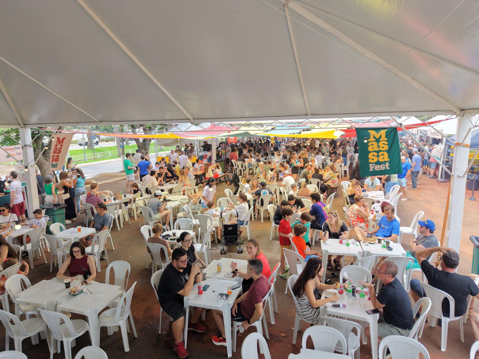 Praça de alimentação sob tenda, com público sentado às mesas
