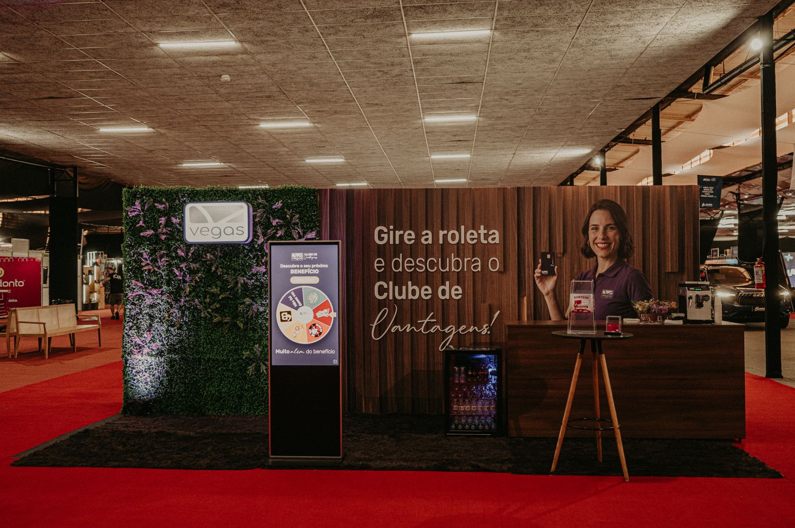 Stand promocional com painel de madeira, totem digital e balcão