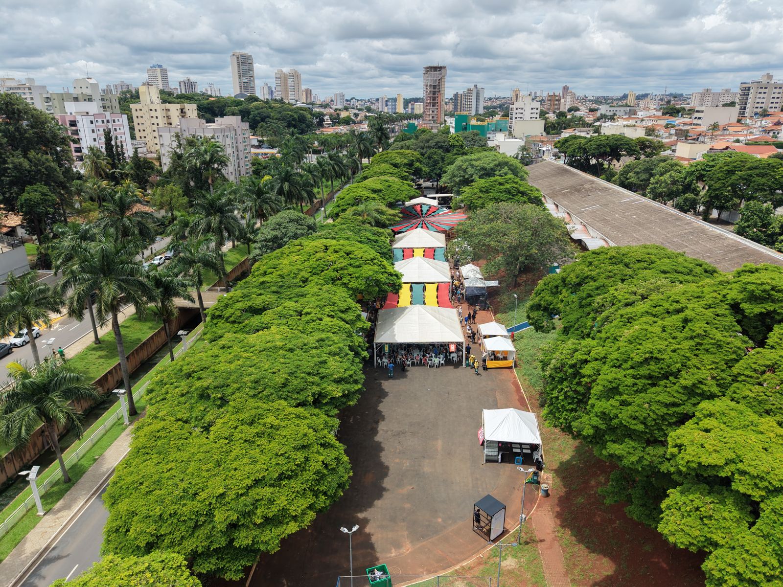 Vista aérea de uma fileira de tendas de feira numa avenida arborizada